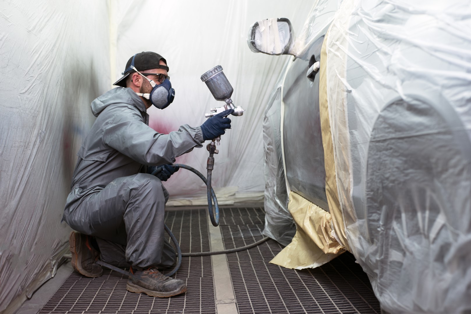 Car painter painting a car door with a mask on, gloves and work clothes